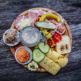 Brett mit regionalen Speisen: Käse, Fleisch, Gemüse und Aufstriche auf Holzunterlage.